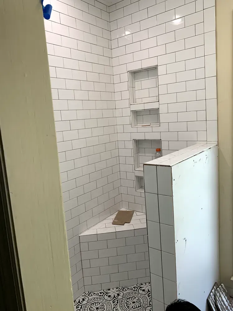 White tiled shower with built-in shelves and a bench. Black and white patterned floor tiles.