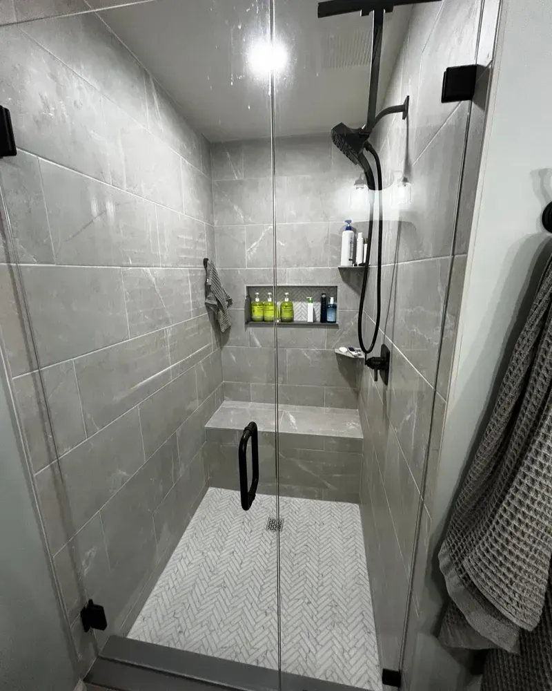 Modern gray-tiled shower with glass doors, built-in seat, and black fixtures.