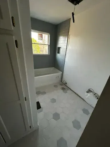 Bathroom under construction, featuring a bathtub, hexagon tile floor, and partially tiled walls.