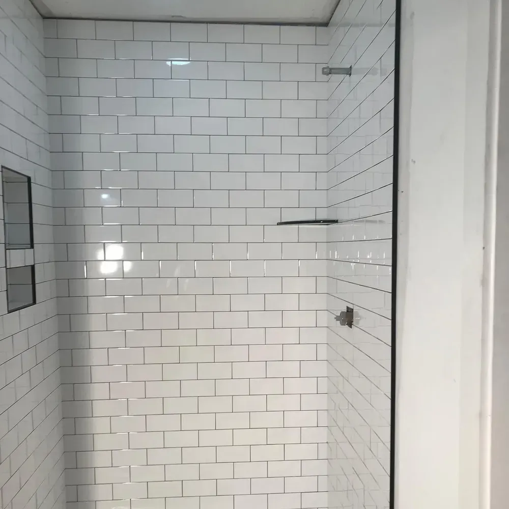 White-tiled shower with glass door and recessed shelves.