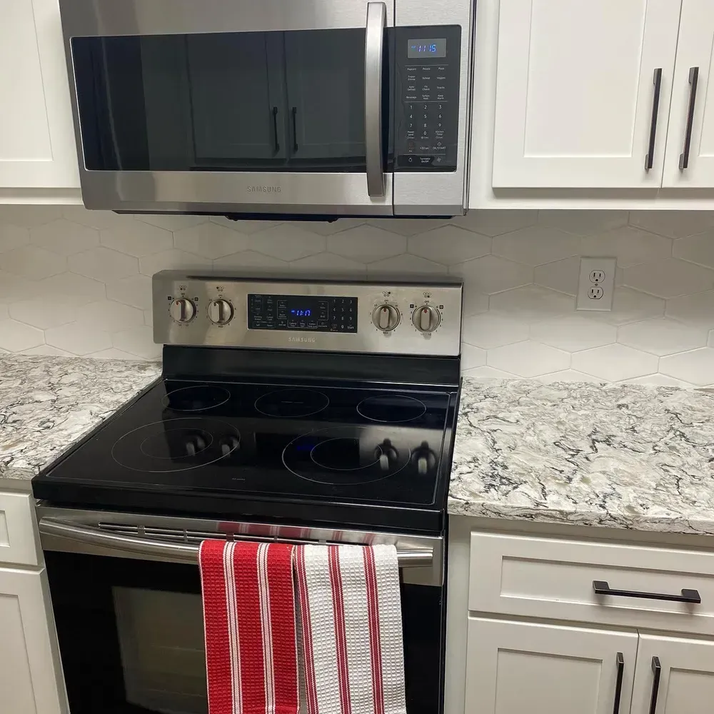Stainless steel kitchen appliances: microwave, range, and white cabinets with speckled countertops.