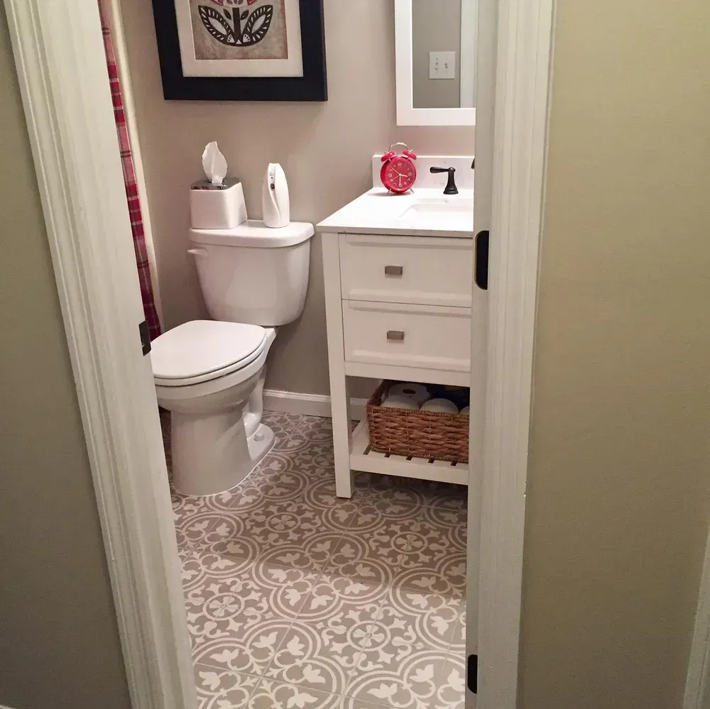 Small bathroom with floral patterned floor, white vanity, toilet, and artwork. Beige and white colors.