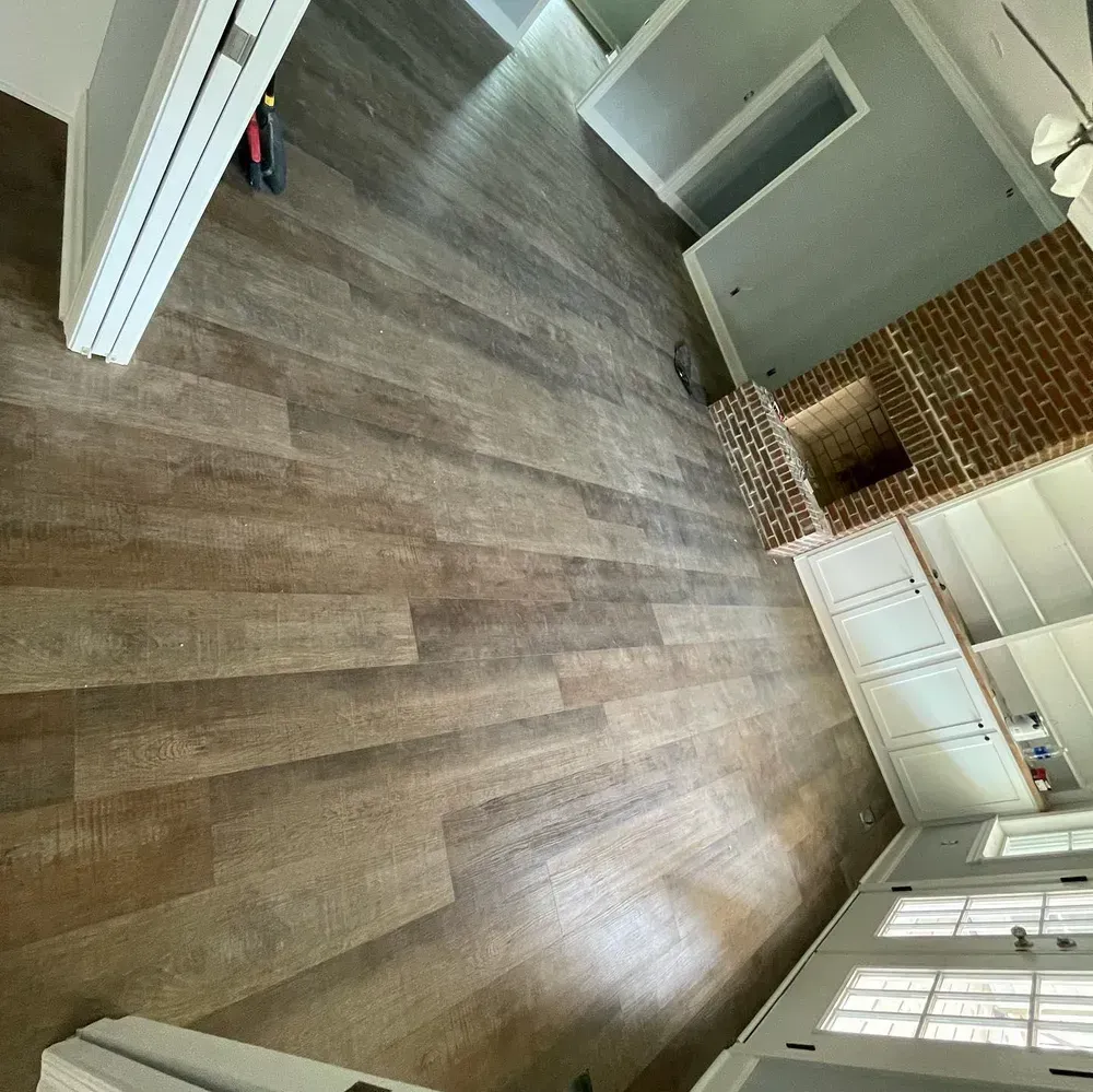 Wooden floors in a room with a brick fireplace and white cabinets.