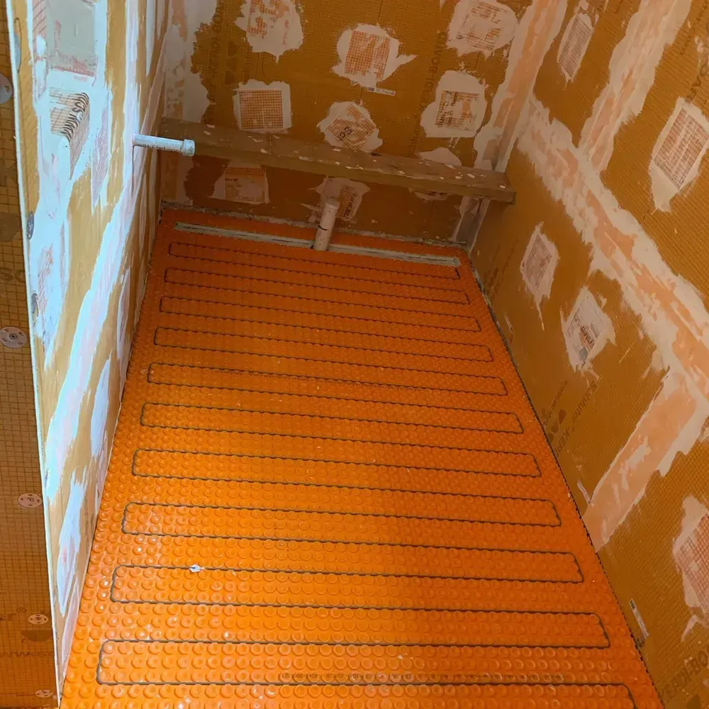 Orange heated floor mat installed in a bathroom, walls show orange and white construction materials.