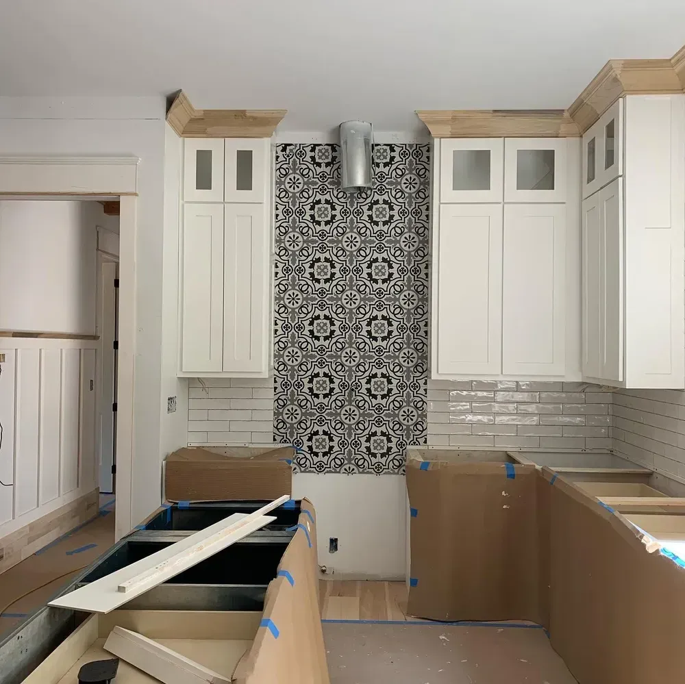 Kitchen under construction with white cabinets, patterned backsplash, and exposed countertops.