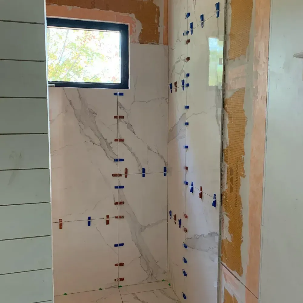 Bathroom with partially tiled walls, spacers visible. Window on one wall.