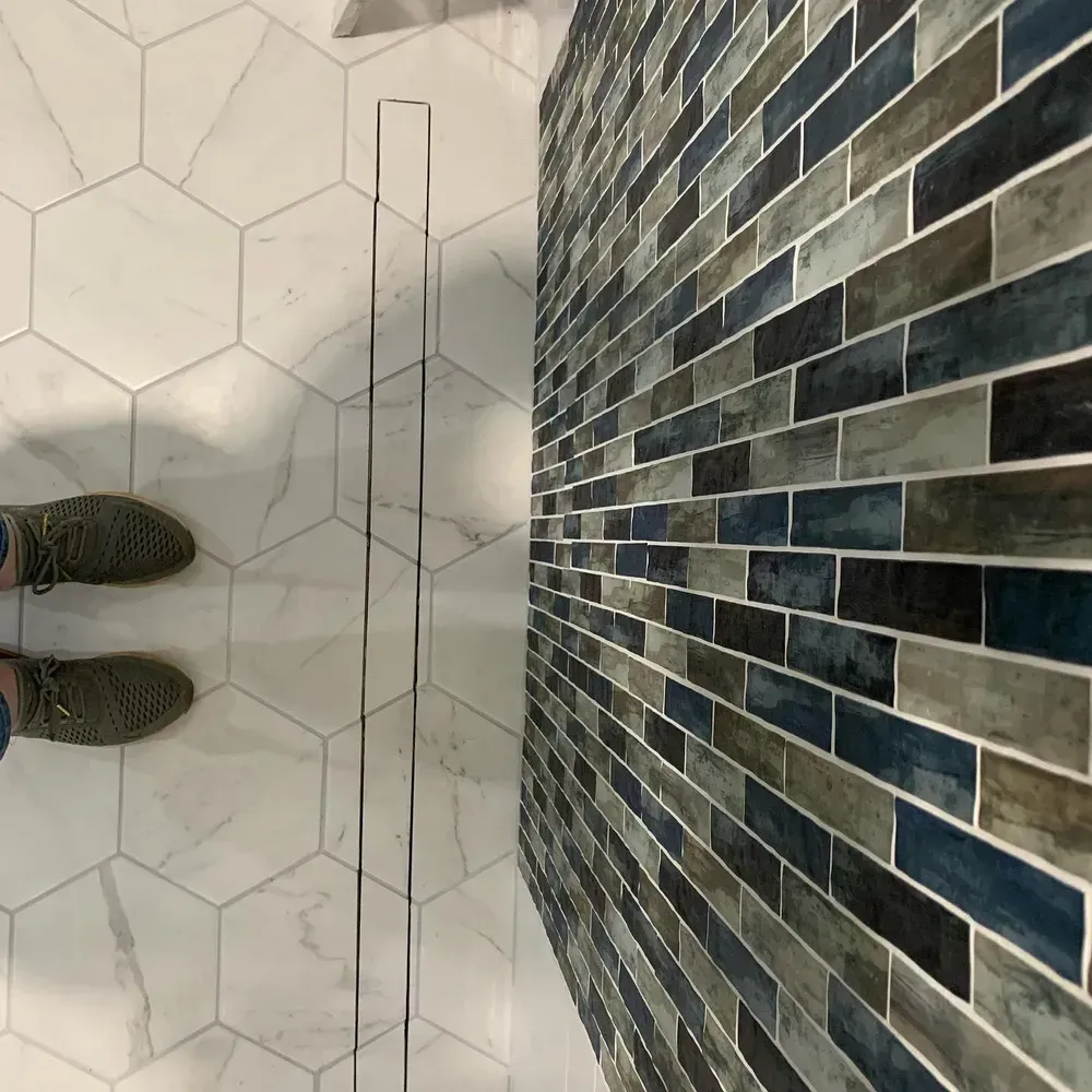 Person in green sneakers stands on white hexagonal tile floor next to blue and gray tiled wall.