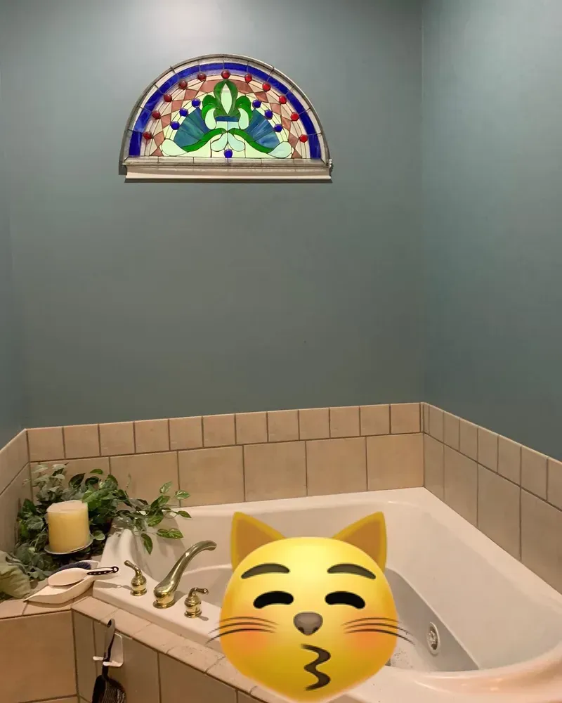 Bathroom with a white bathtub, blue walls, and a stained glass peacock window.