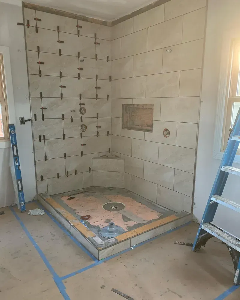 Shower stall under construction, with beige tiles on walls. Tiles are held with spacers.