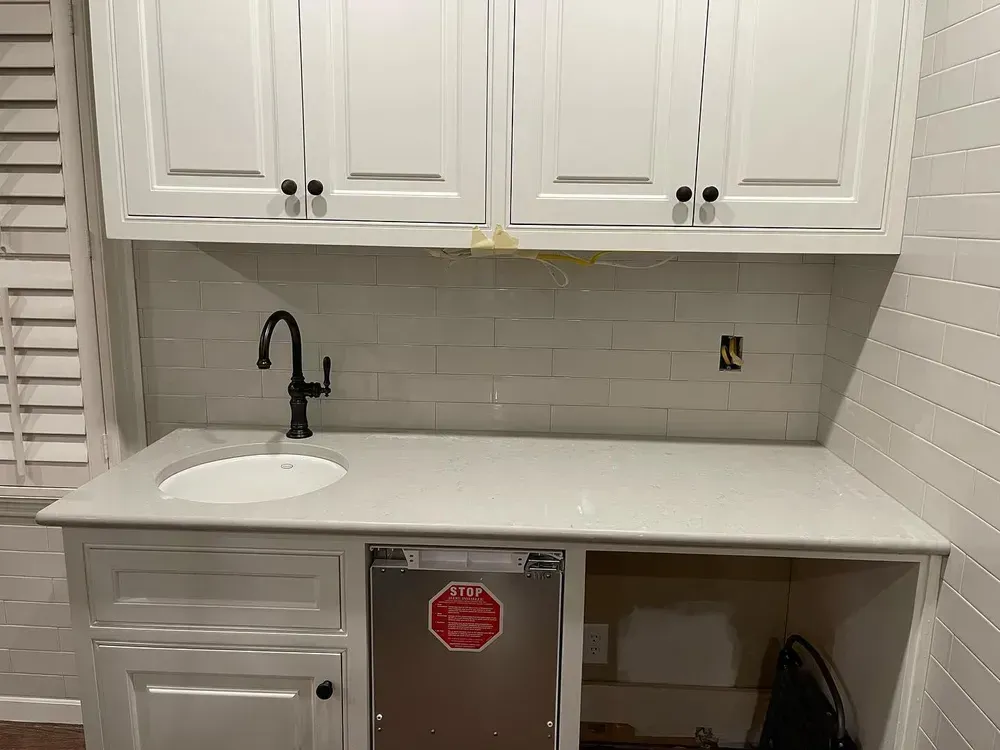 White kitchen cabinetry with a countertop, sink, faucet, and an under-counter ice maker.