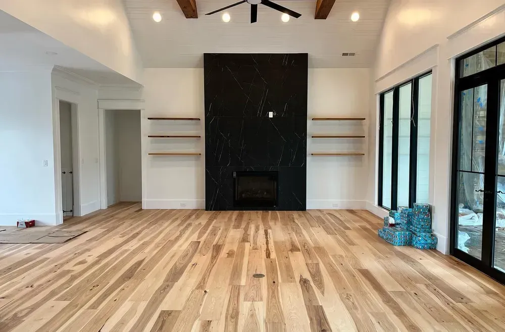 Empty living room with light wood floors, black fireplace, and large windows.
