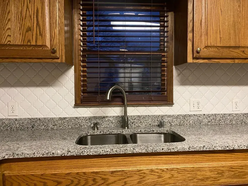 Kitchen sink with a window, wooden cabinets, and granite countertop.