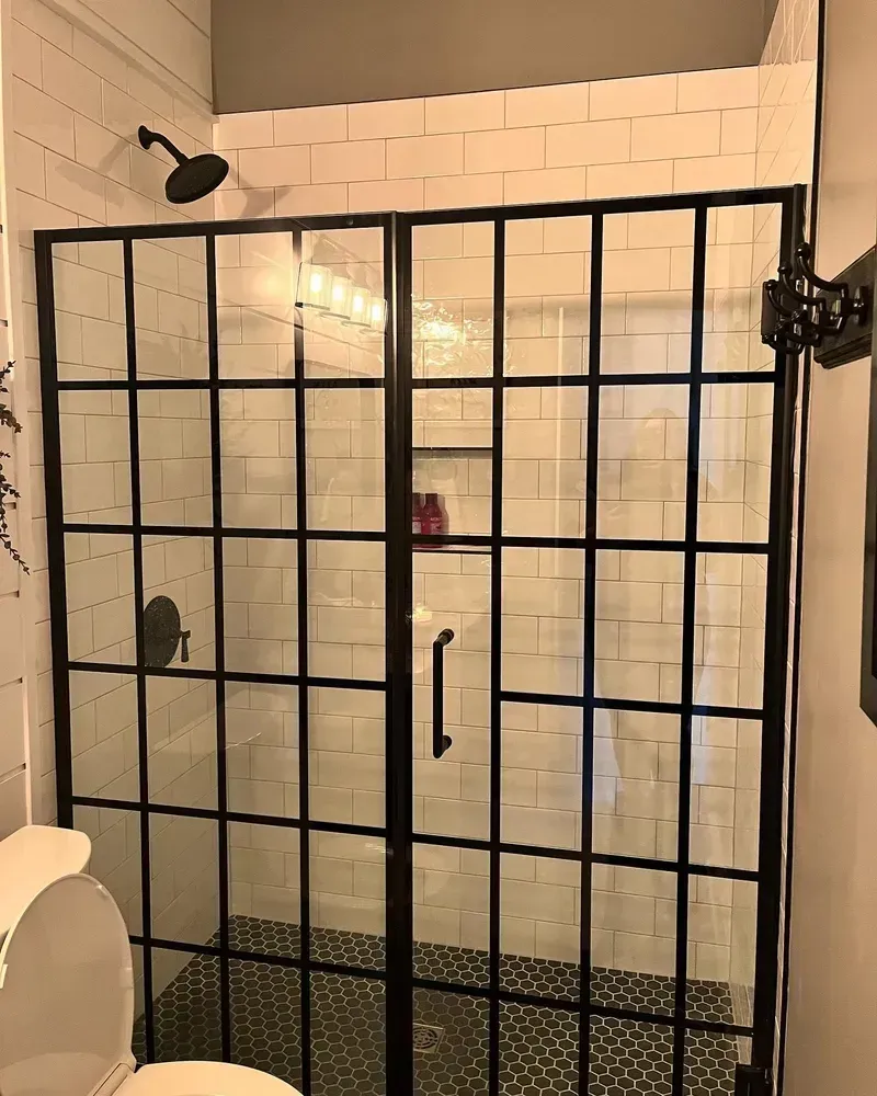 Black-framed shower with grid-like glass doors. Black showerhead and hardware against white tiled walls.