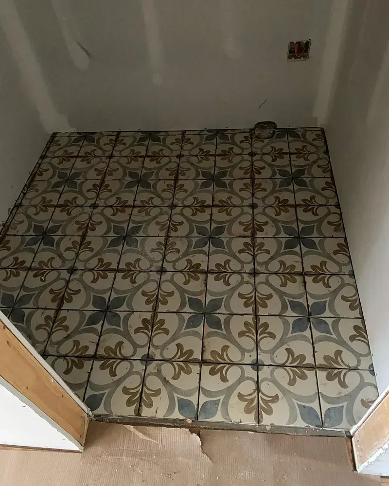 Floor tiled with patterned blue, tan, and gray tiles in a small room with drywall walls.