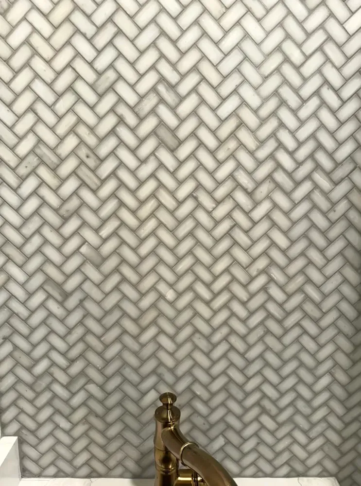 Herringbone tile wall with gold faucet.