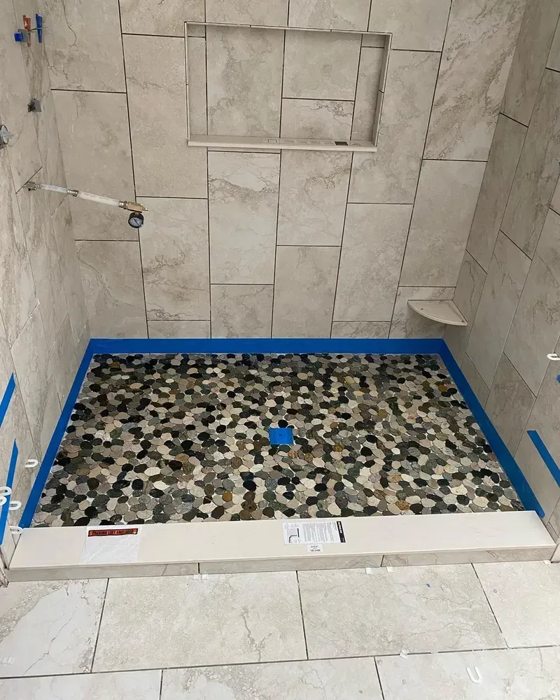 Shower under construction with tiled walls, stone floor, and a recessed shelf.