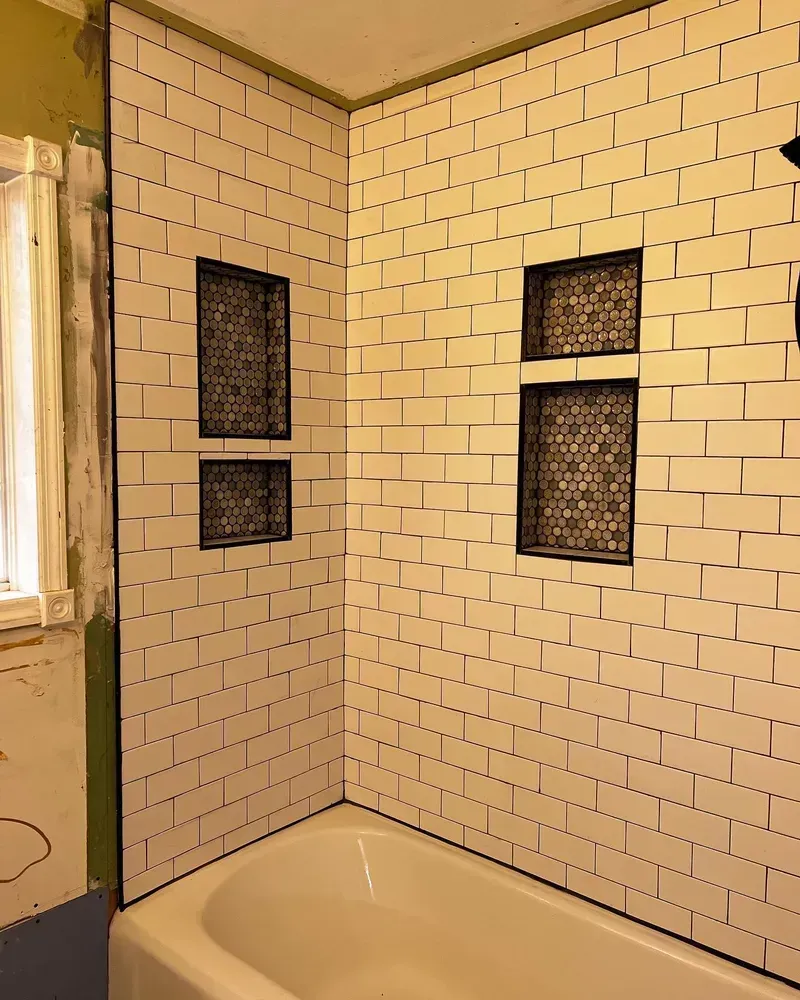 Bathroom wall tiled with white subway tile. Two recessed shelves with mosaic tile. Bathtub visible.