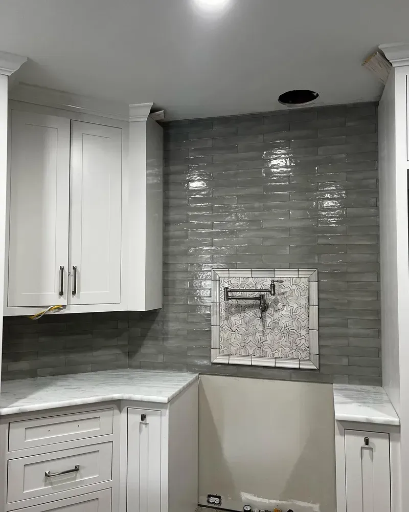 Kitchen remodel: gray tiled backsplash, white cabinets, marble countertops, and a pot filler.