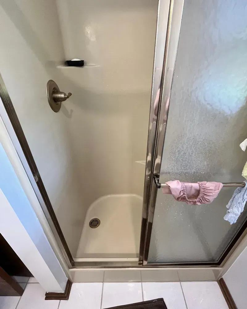 A small, beige-walled shower stall with a curved base, sliding glass doors, and a faucet.