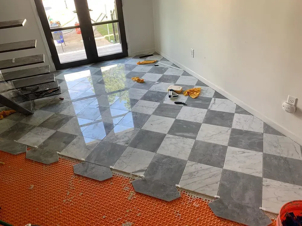 Checkerboard tile floor installation in a room with a staircase and a doorway to outside.