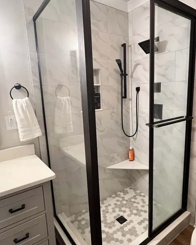 Modern bathroom with a glass shower, marble tile, and black fixtures.