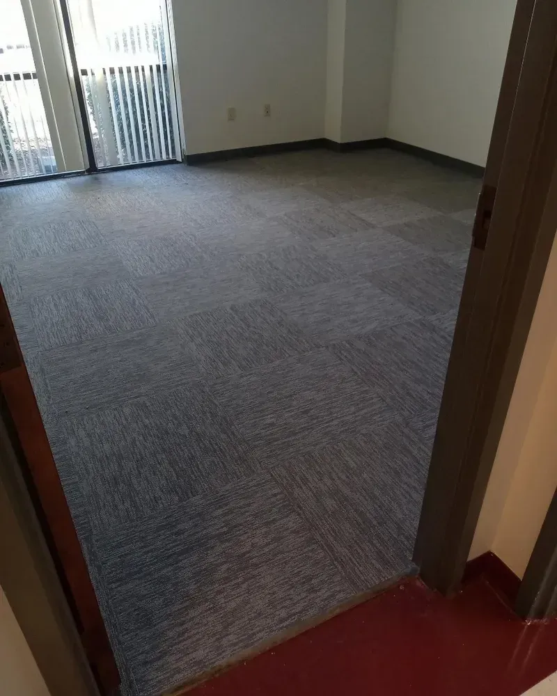 View from a doorway into an empty room with blue carpet and a balcony.