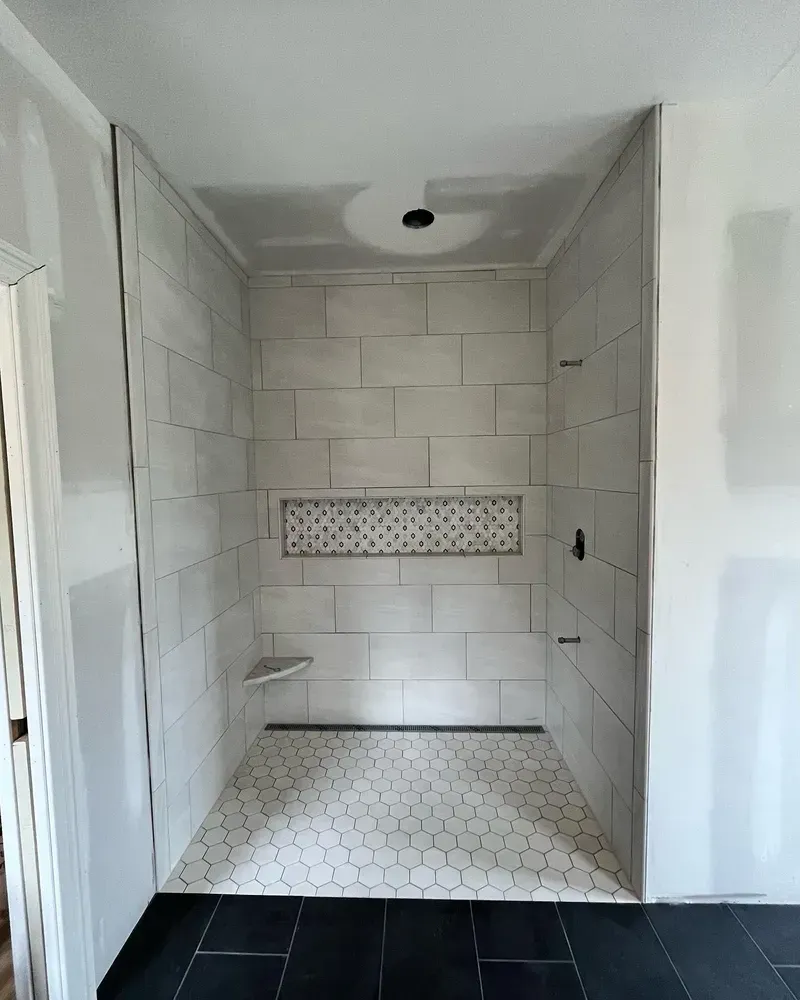 Bathroom shower with tiled walls and floor, recessed shelf, and black hexagon floor tiles.