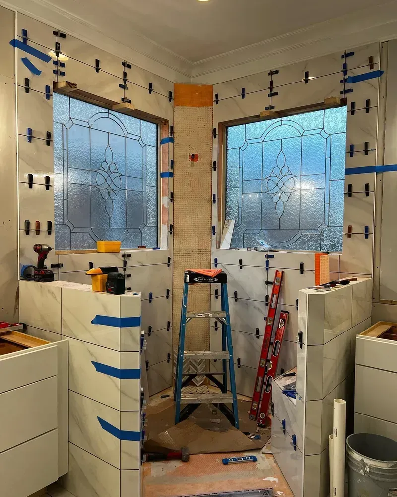 Bathroom under construction with tile partially installed; windows visible, tools present.