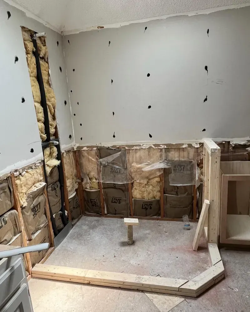 Bathroom undergoing renovation; drywall removed, revealing insulation and framing. Wooden support structure is visible.