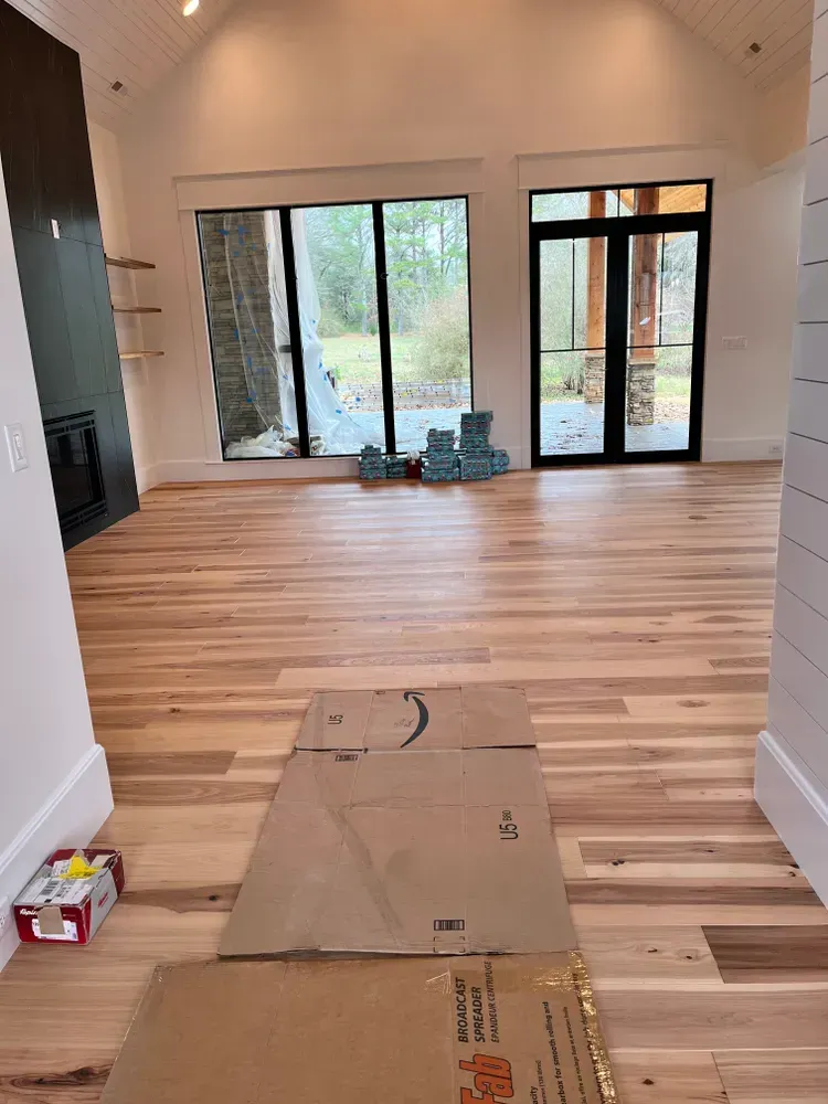 Hardwood floor in a bright room with large windows, fireplace, and an Amazon box on the floor.