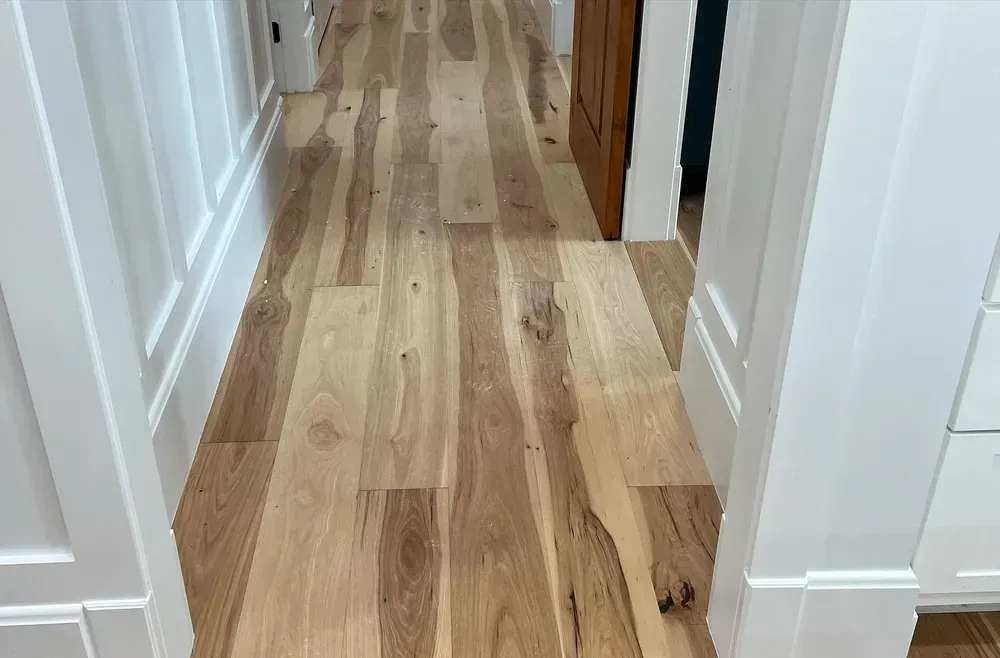 Wooden hardwood flooring in a hallway, framed by white trim and doors.