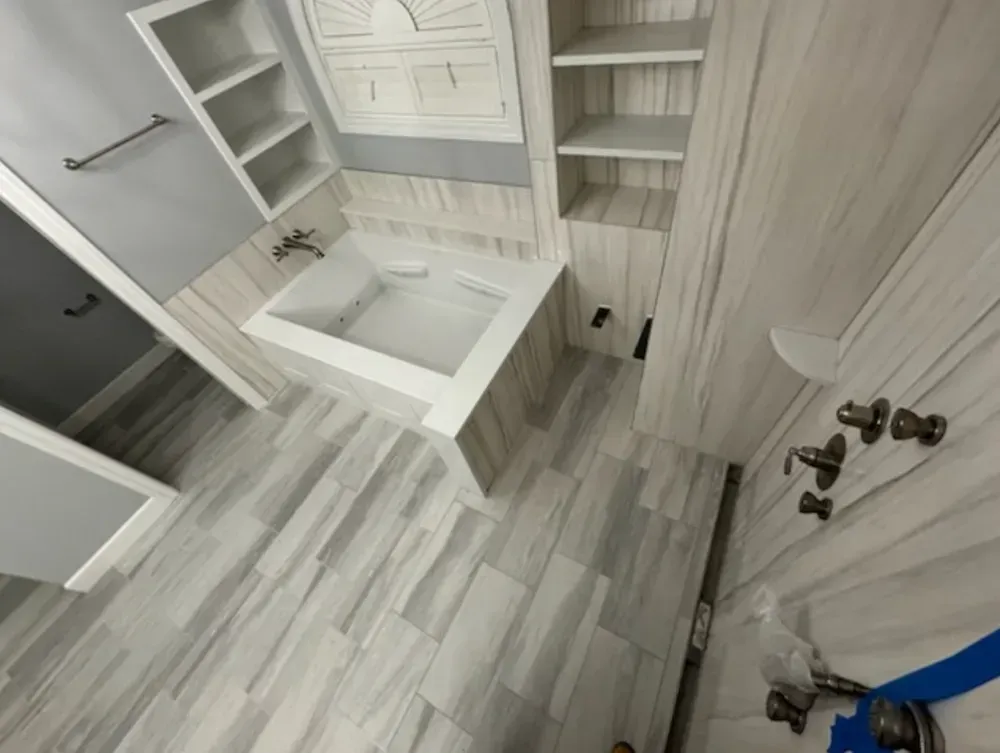 Bathroom with a white bathtub and shelves, light gray wood-look tile on the floor and walls.