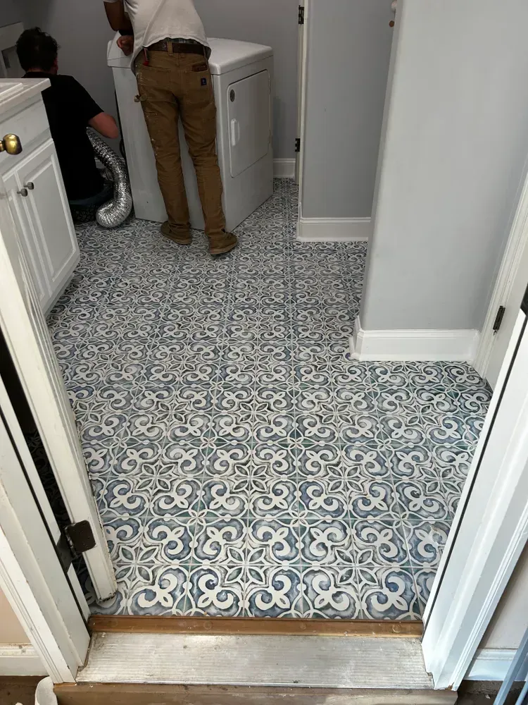 Laundry room with ornate blue and white tiled floor, two people, one near the dryer.