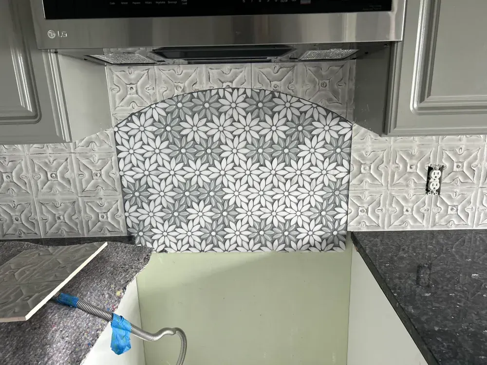 Kitchen backsplash with daisy pattern and decorative tiles under a range hood, gray cabinets.