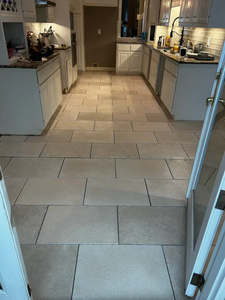 Kitchen with light-colored tile flooring, white cabinets, and countertops. A doorway is in the foreground.