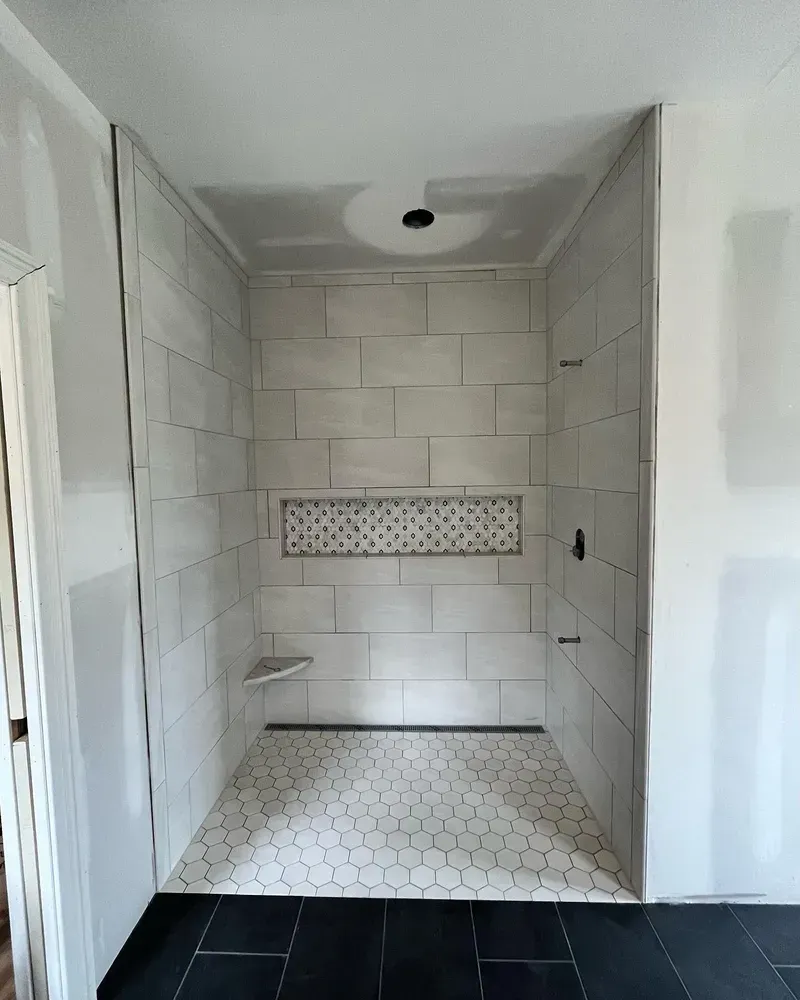 Newly tiled shower stall with gray and white tiles, a built-in shelf, and a recessed soap niche.