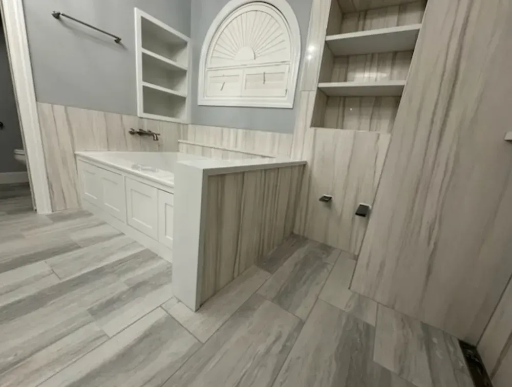 Bathroom with white cabinetry, shelves, and gray wood-look tile.