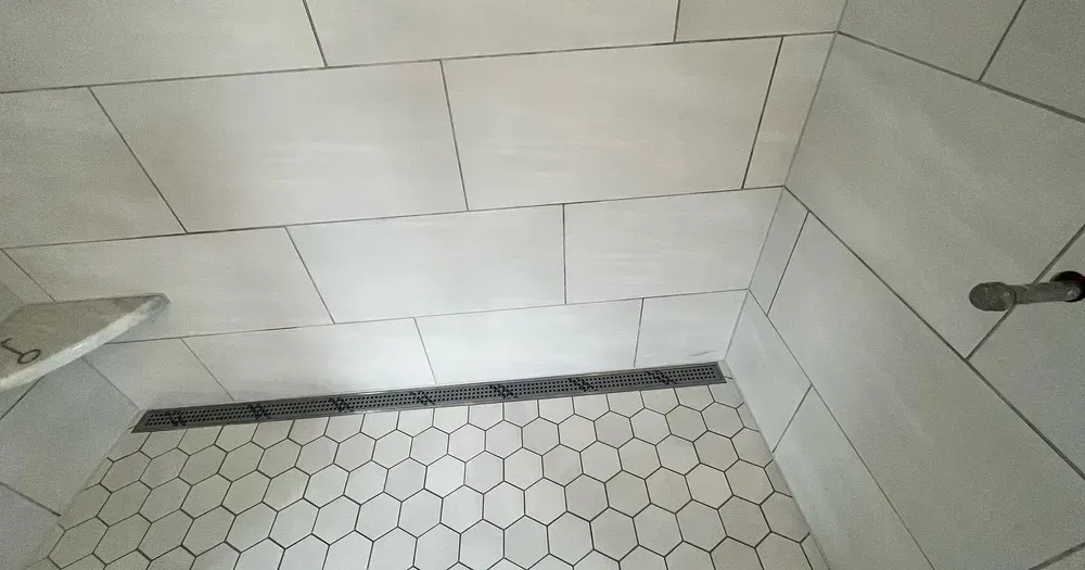 White tiled shower with a hexagonal tile floor and a linear drain.