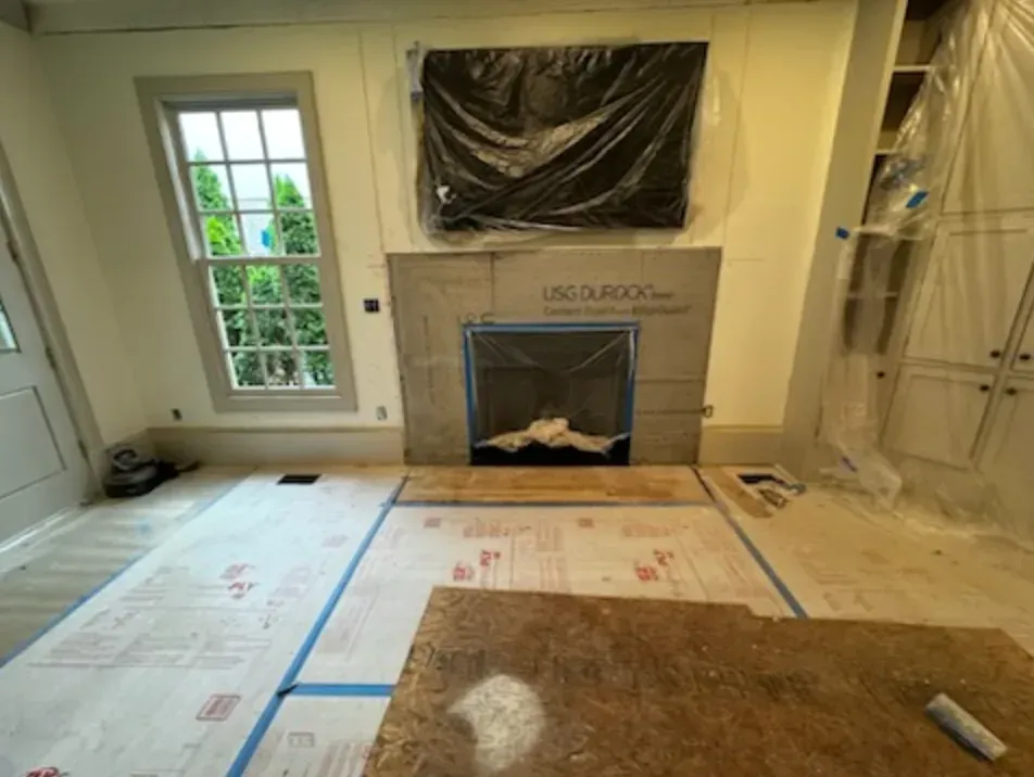 Room under renovation with fireplace, window, and plastic sheeting covering items.