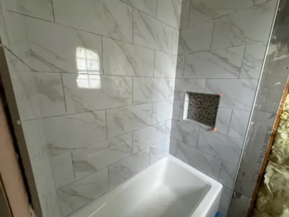Tiled shower surround with white marble-look tiles, a built-in niche, and a white bathtub.