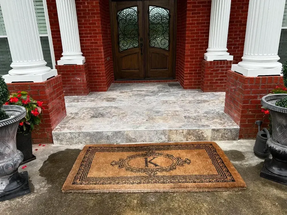 Front entrance with brick wall, white columns, double doors, and a welcome mat with a large