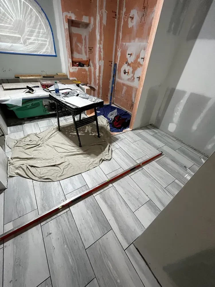 Bathroom renovation with new gray tile floor. Tools on table and unfinished walls in background.