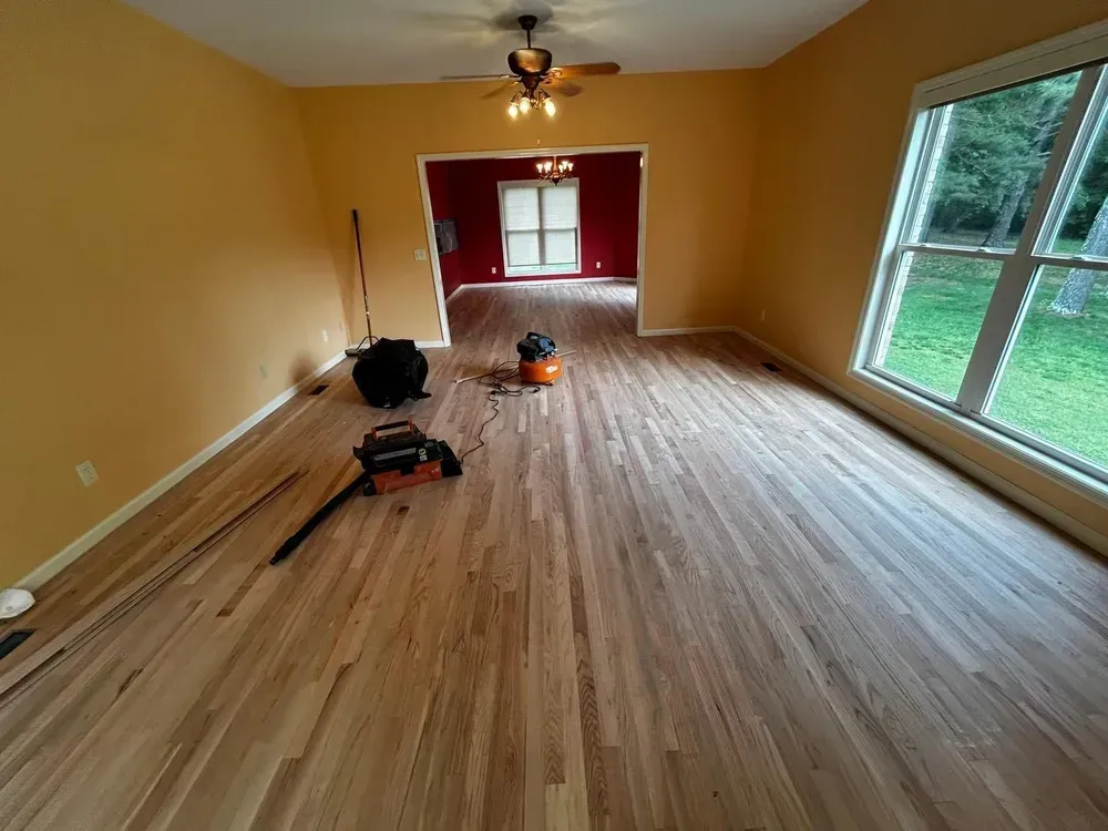 Wooden floors being installed in a room with yellow walls and a view of greenery.