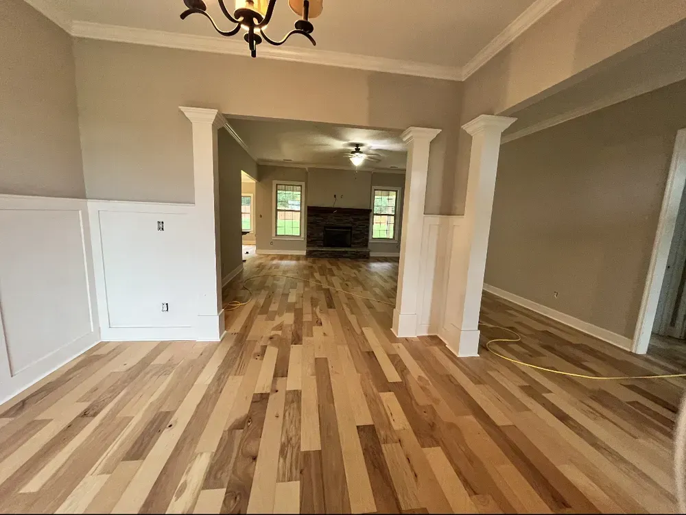 Interior of a home with hardwood floors, light gray walls, and white trim. Opening to a living area with fireplace.