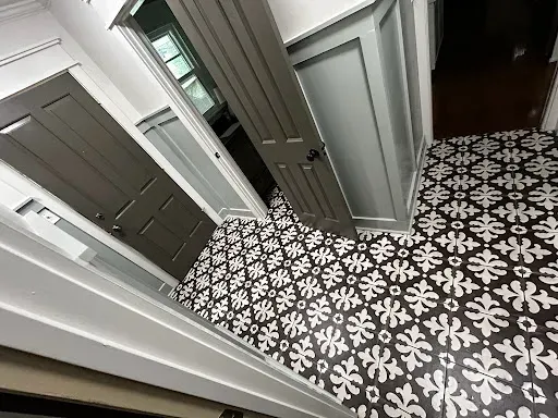 Hallway with patterned black and white floor tiles, gray doors, and white paneled walls.