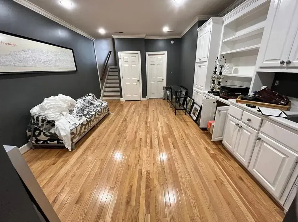 Wooden-floored room with white cabinets, dark walls, sofa, and stairs leading up.