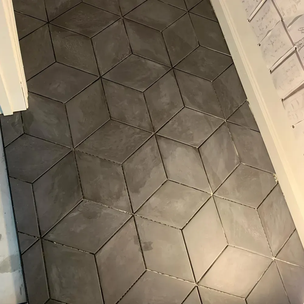 Gray tiled floor with diamond-shaped pattern, set between white door frames and brick wall.