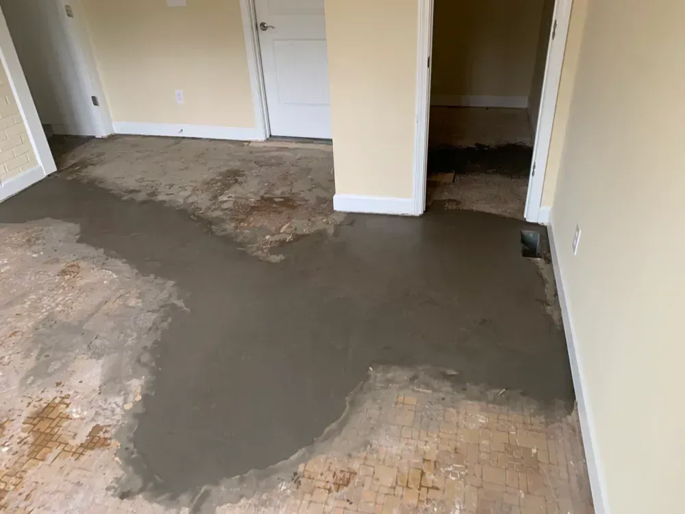Room with concrete patching on the floor; light yellow walls, white doors, and doorways.