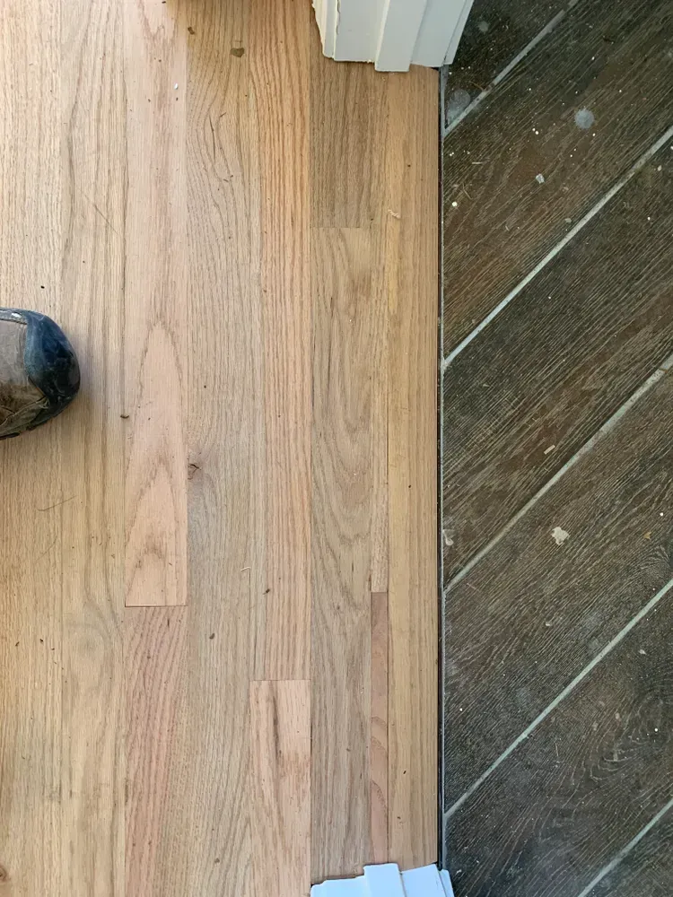 Light wood floor next to dark diagonal wood floor, separated by a thin strip, foot in view.
