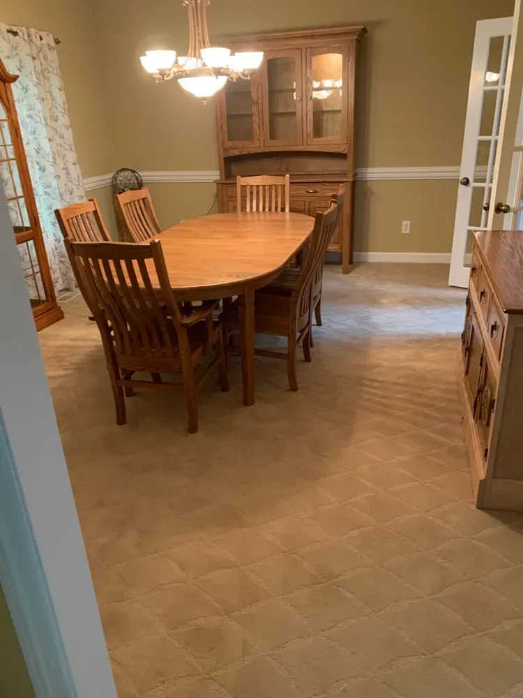 Dining room with wooden table and chairs, buffet, and hutch on patterned carpet.
